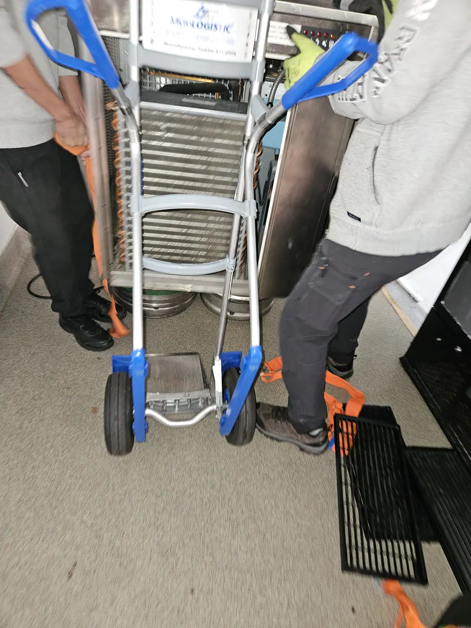 Two movers moving a white goods appliance with a stair trolley.