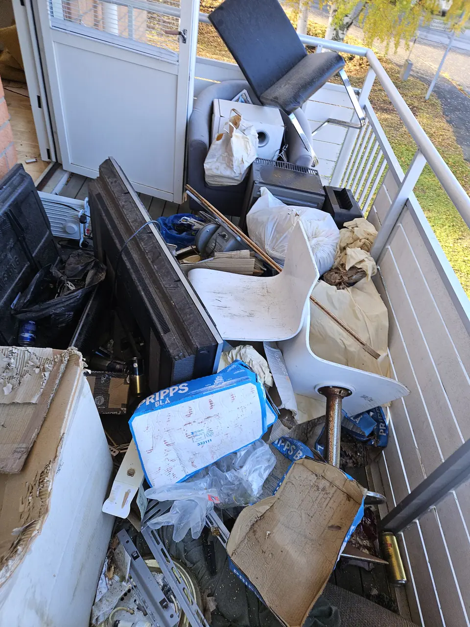 A balcony full of furniture, boxes and rubbish before clearance.
