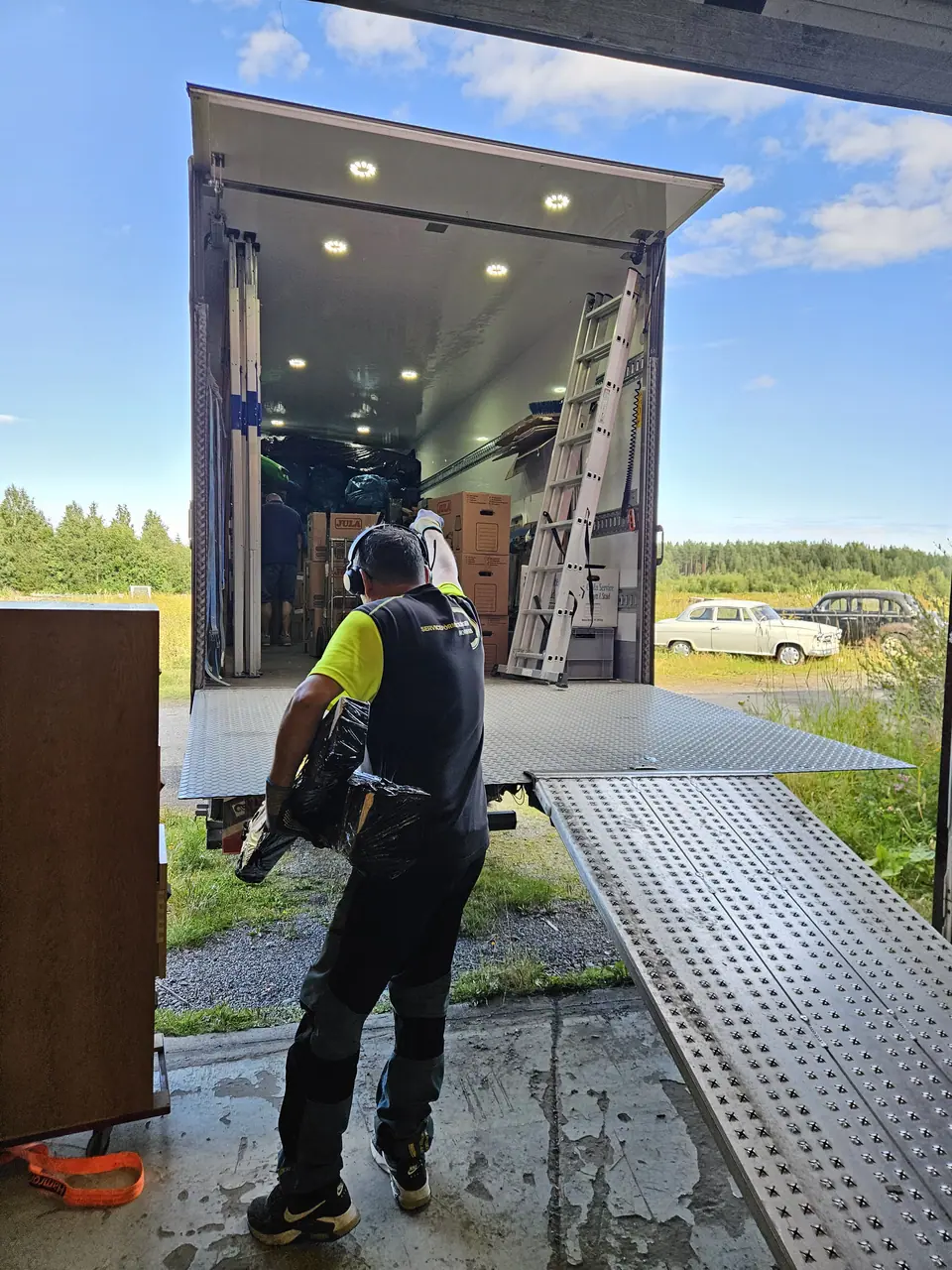 A mover in a high-visibility vest loading furniture into a removal van over a ramp.